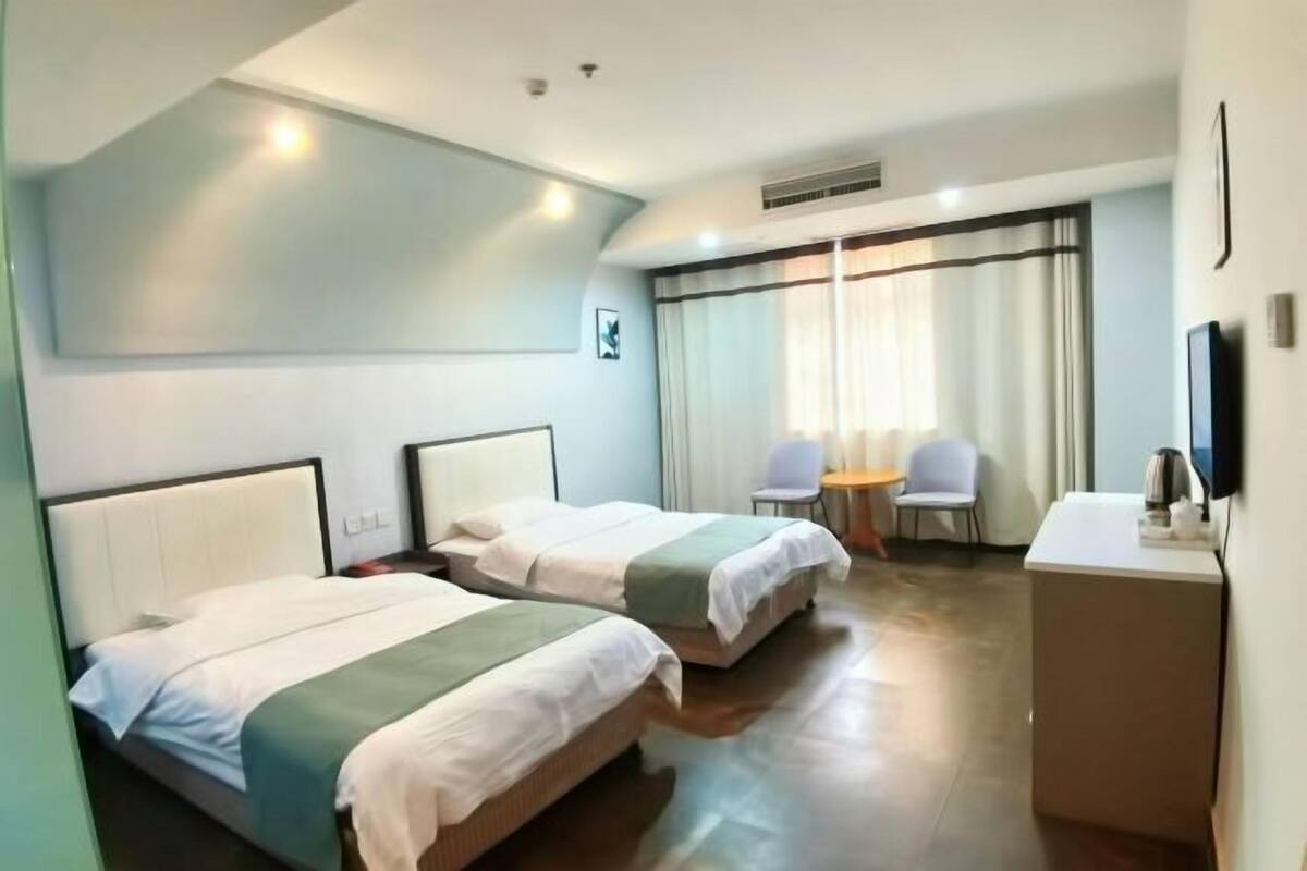A hotel room with two beds, a desk, a chair, a TV, and a window with curtains.