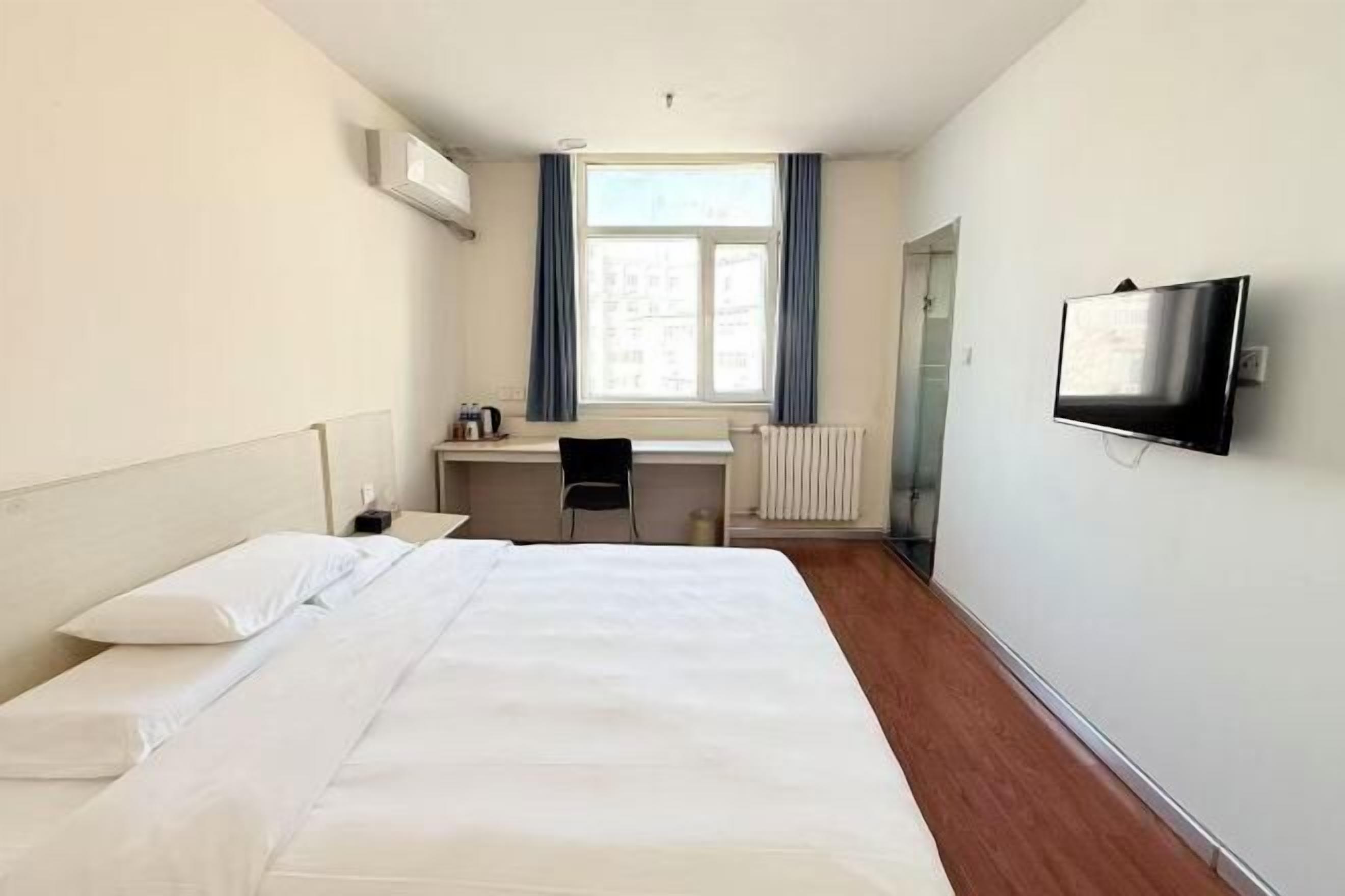 A hotel room with a bed, a desk, a chair, a TV, and a window with curtains.