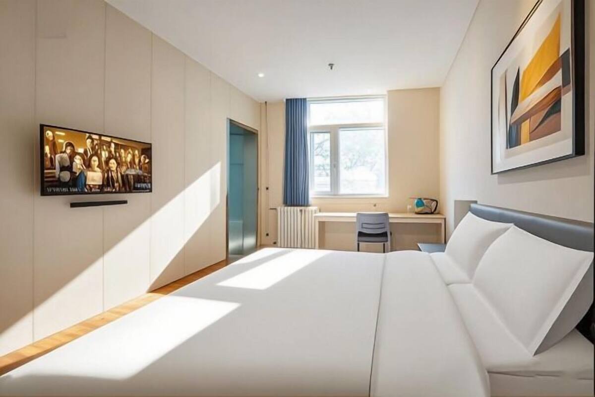 Une chambre d’hôtel moderne équipée d’un lit, d’un bureau, d’une chaise, d’une télévision et d’une fenêtre.