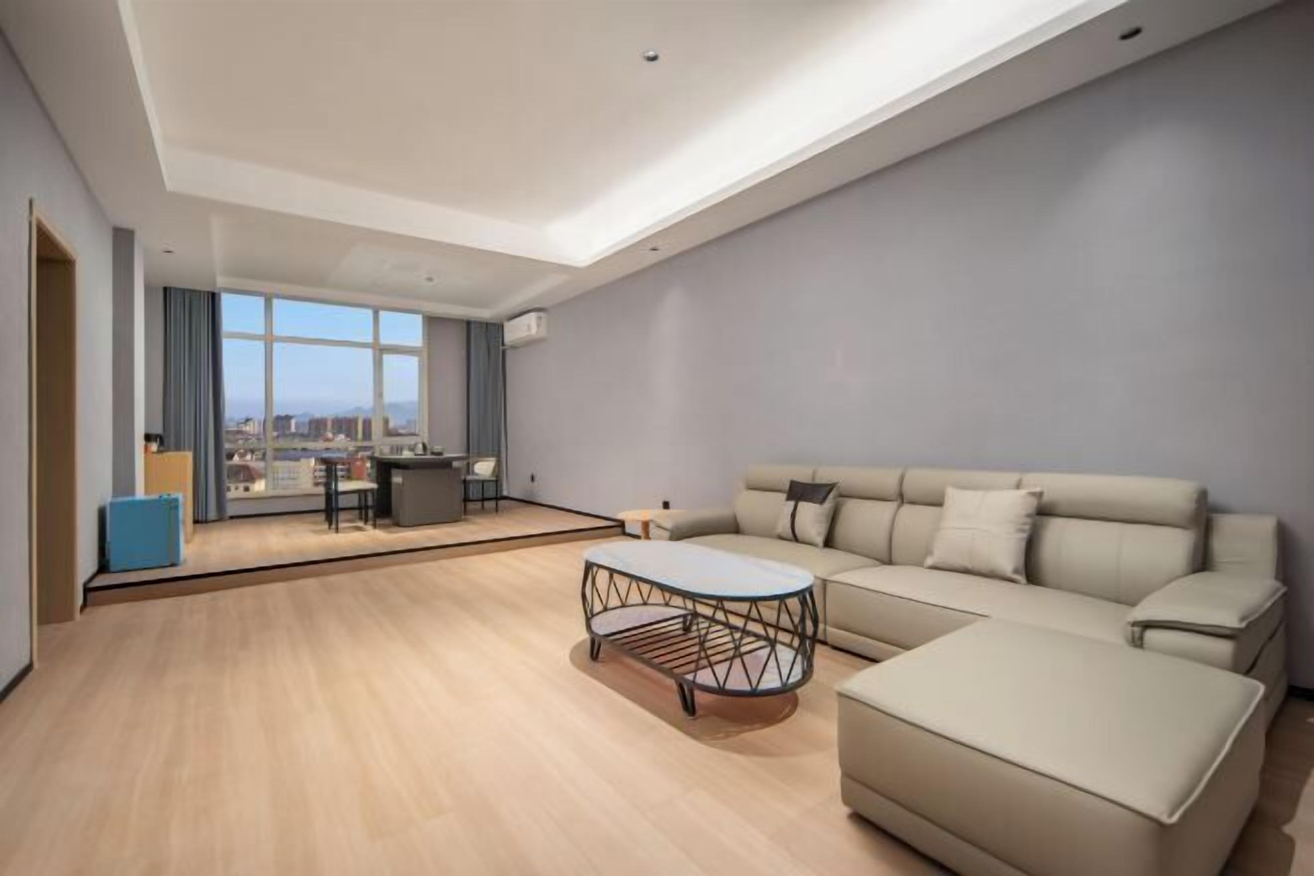 A modern living room with a large sofa, a coffee table, and a view of the city through large windows.