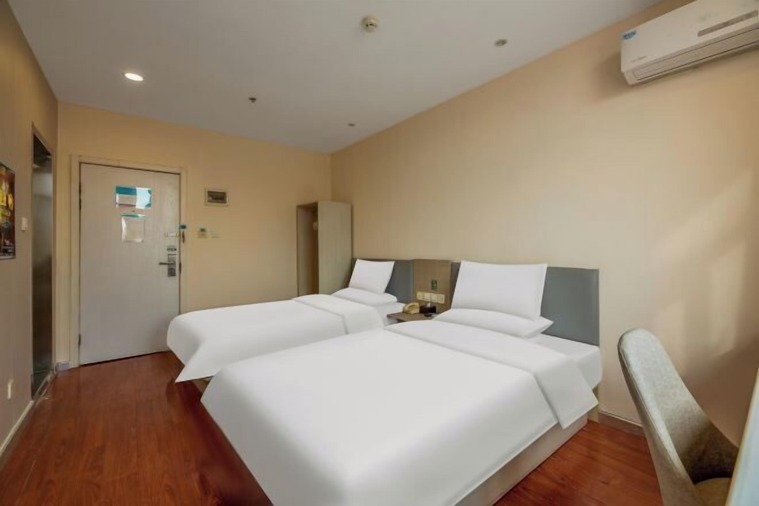 A hotel room with two beds, a wooden floor, a door, and an air conditioning unit.