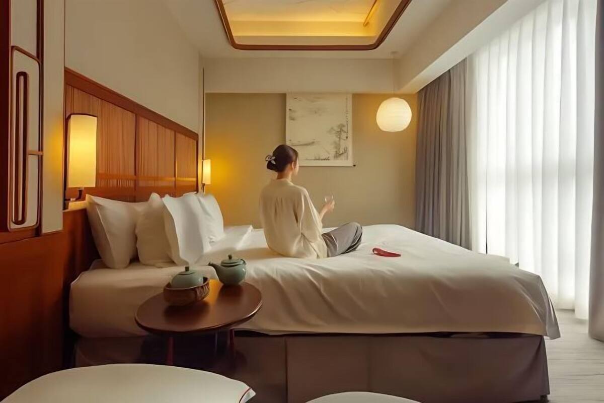 Une chambre d’hôtel comprenant un lit, une table de chevet, une lampe, une œuvre d’art et une vue sur l’extérieur.