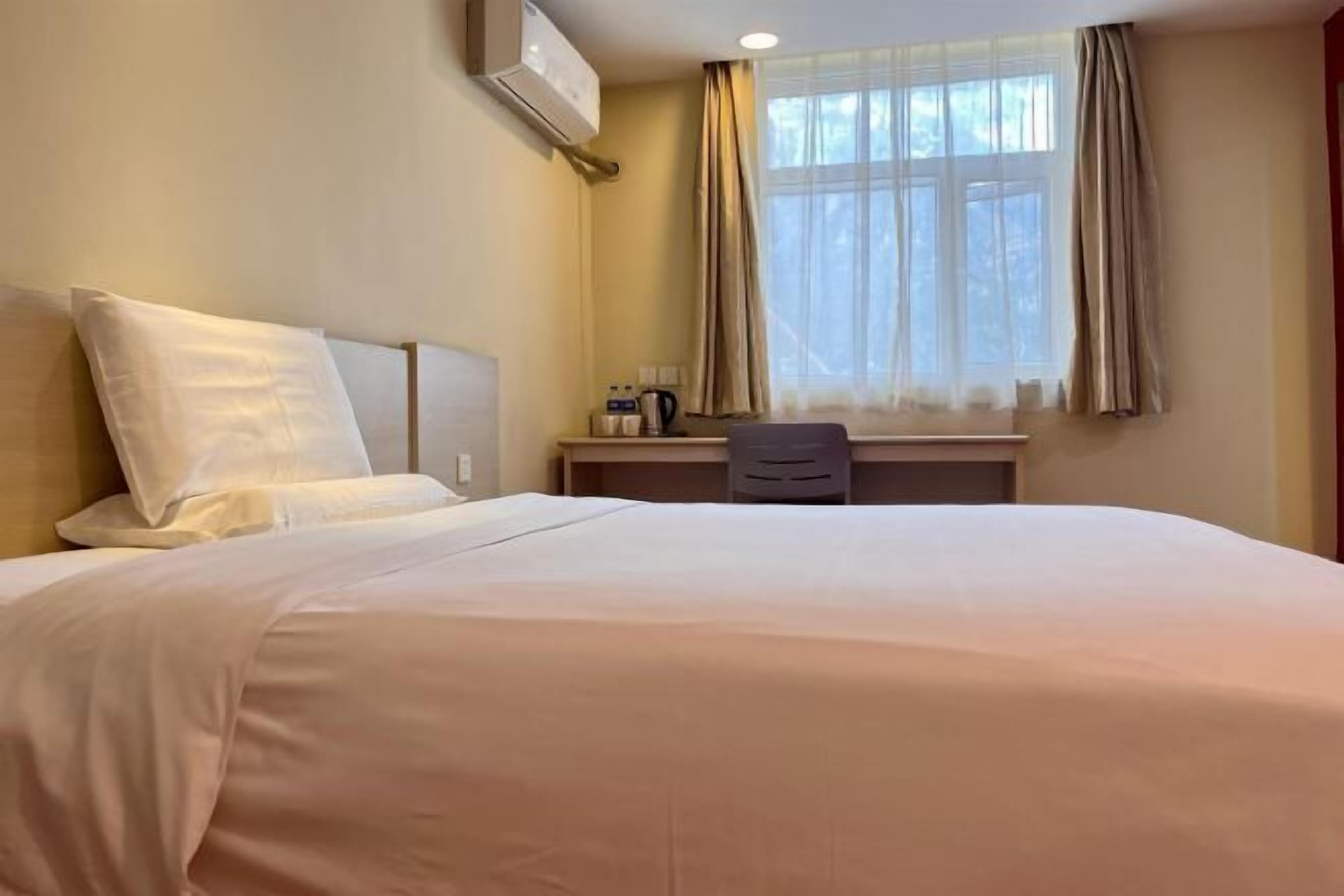 A hotel room with a bed, a desk, a chair, and a window with curtains.