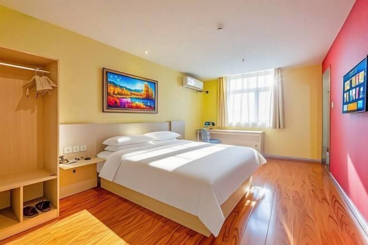 Une chambre d’hôtel comprenant un lit, une armoire, un tableau, une fenêtre avec des rideaux et un téléviseur fixé au mur.