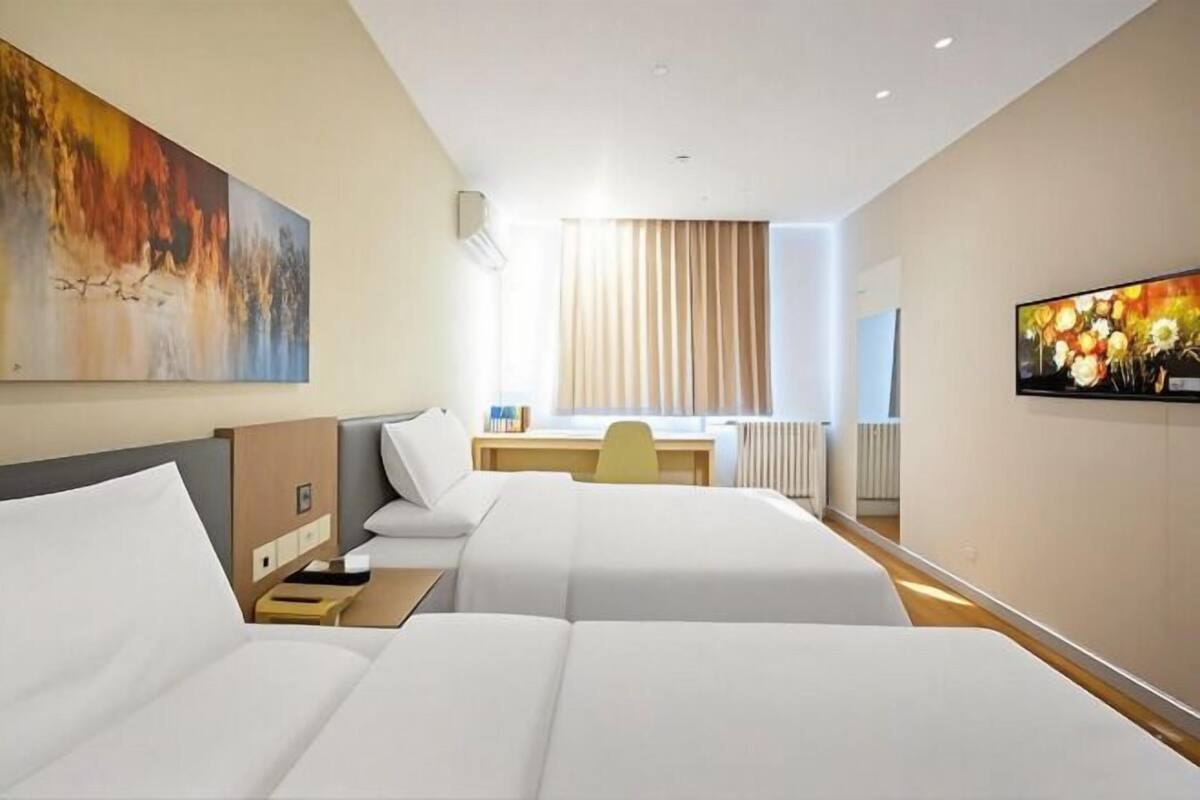 Une chambre d’hôtel avec deux lits, un bureau, une chaise et des œuvres d’art accrochées aux murs.