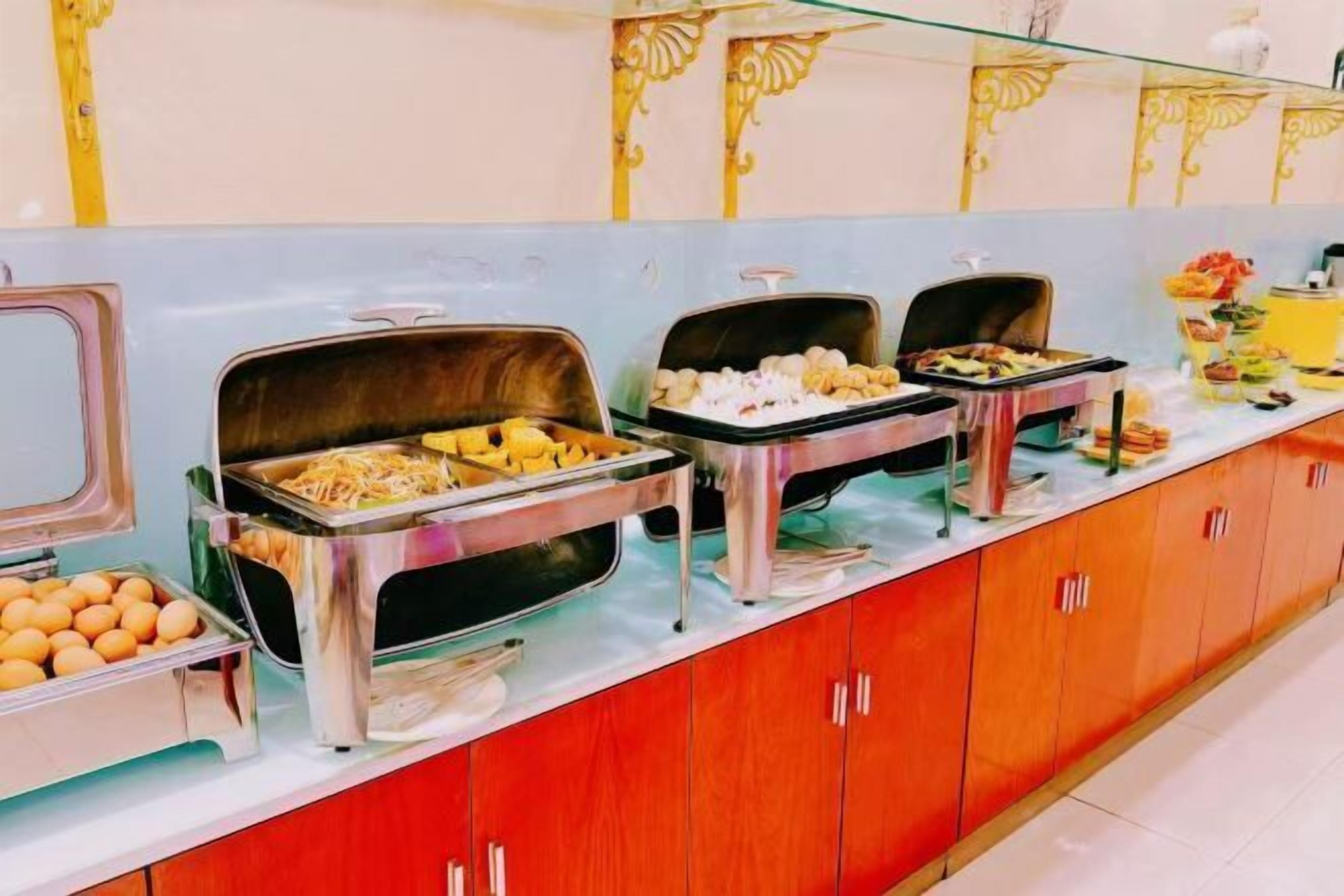 Montaje tipo bufé con diversos alimentos en recipientes metálicos, una vitrina de vidrio y una barra con detalles decorativos.