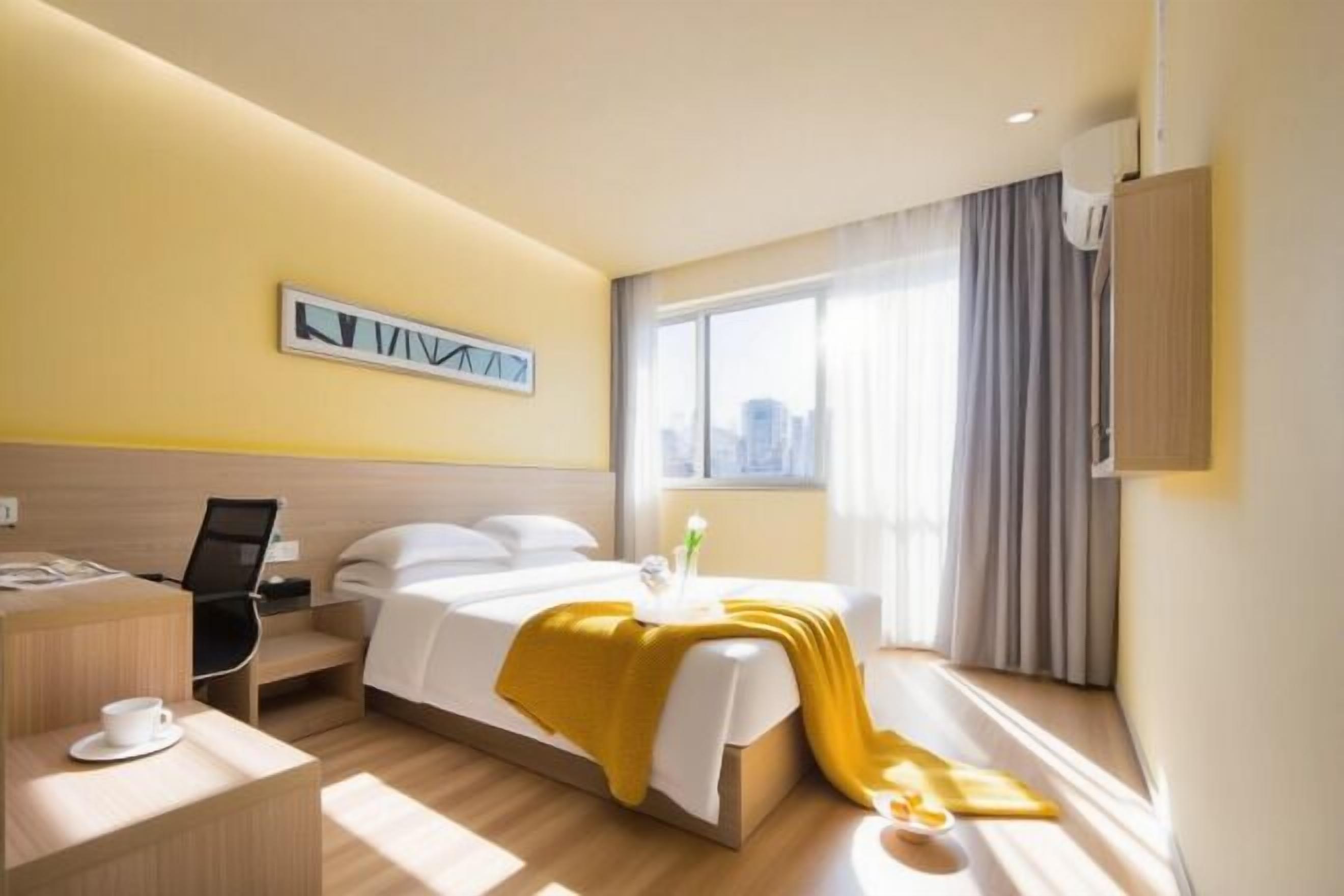 Ein Hotelzimmer mit Bett, Schreibtisch, Stuhl, einem Fenster mit Vorhängen und Blick auf die Stadt.