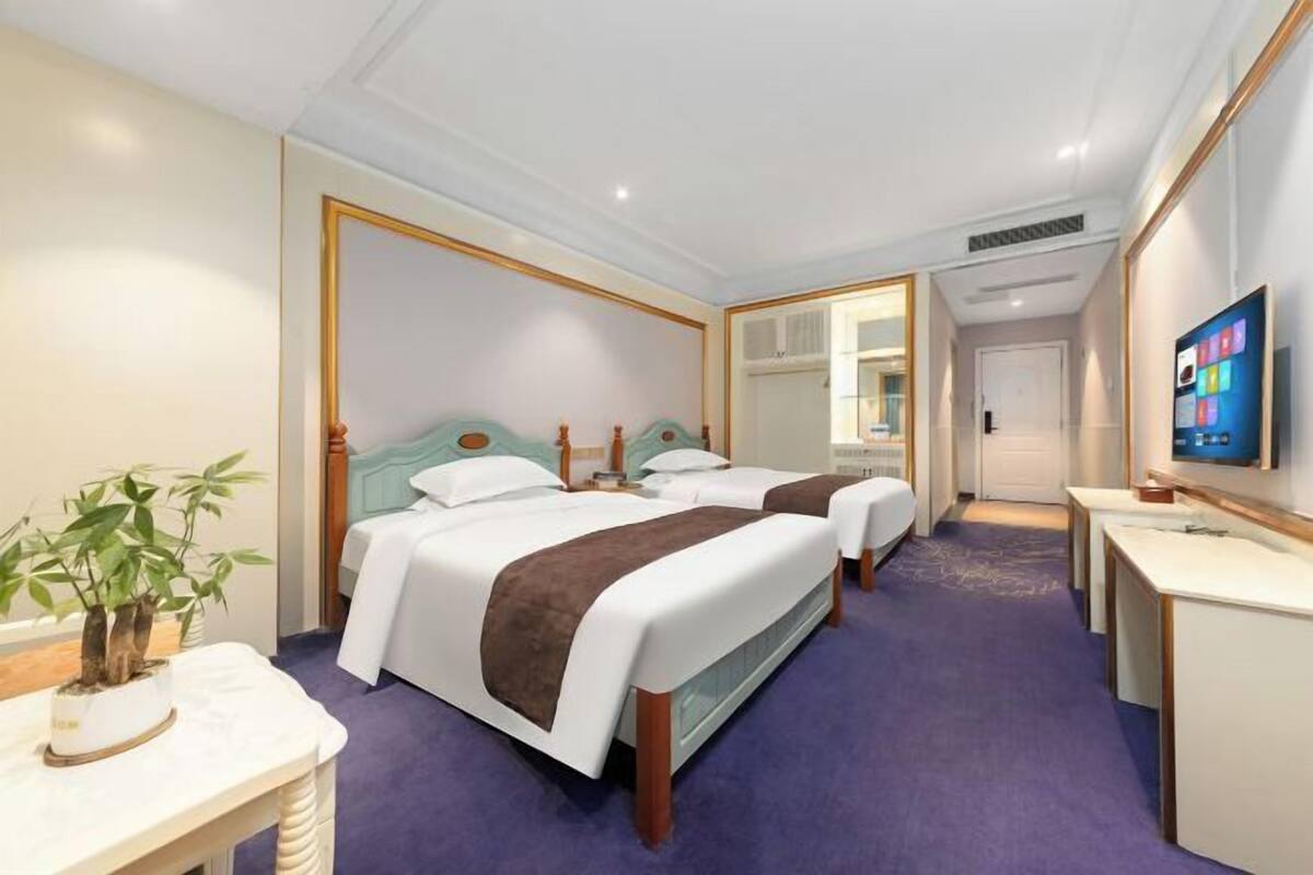 Ein Hotelzimmer mit zwei Betten, einem Fernseher, einem Schreibtisch und einem Spiegel.