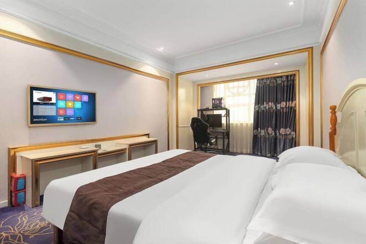 Ein Hotelzimmer mit Bett, Schreibtisch, Stuhl, Fernseher und einem Fenster mit Vorhängen.