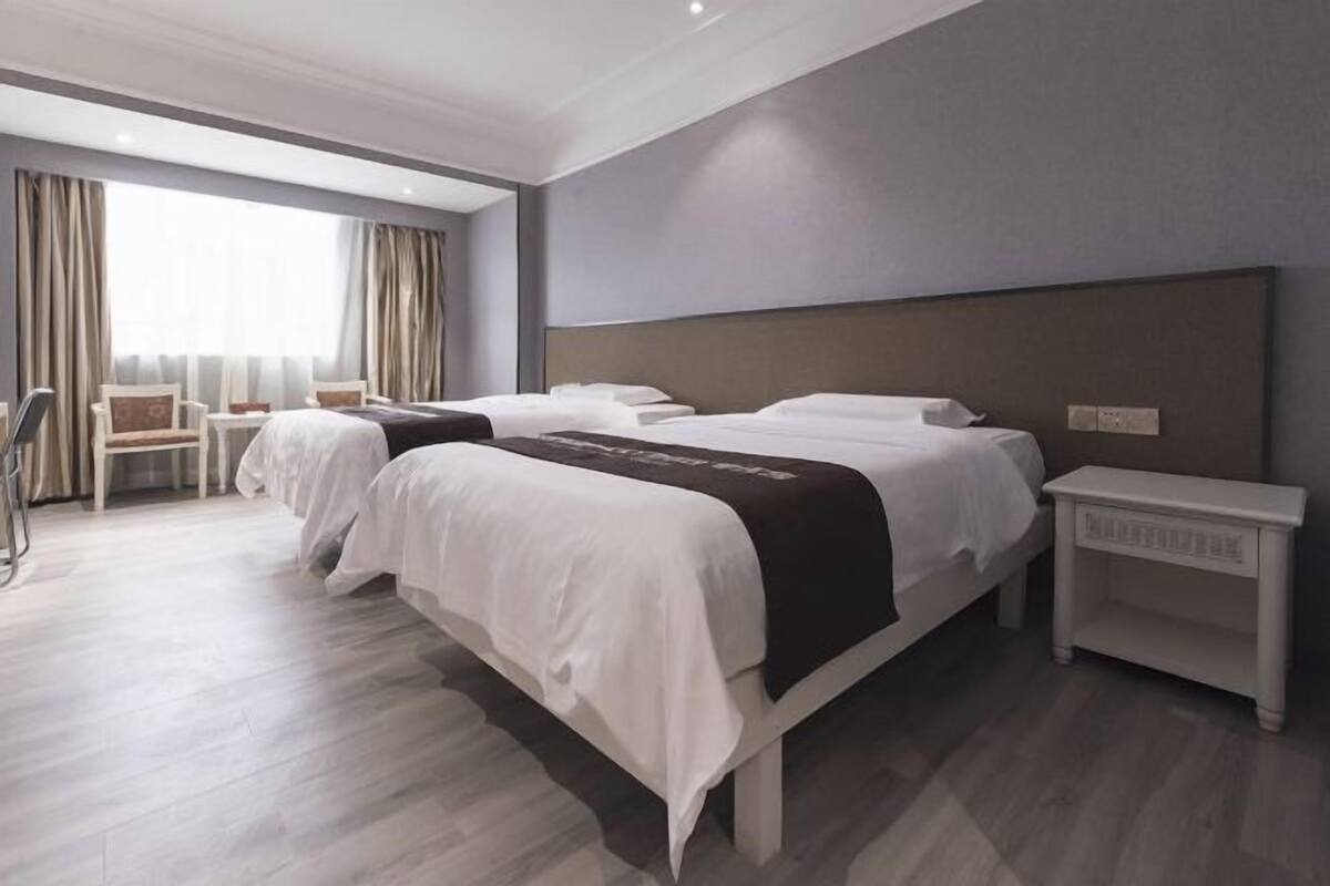 Ein Hotelzimmer mit zwei Betten, einem kleinen Tisch, einem Stuhl und einem großen Fenster mit Vorhängen.