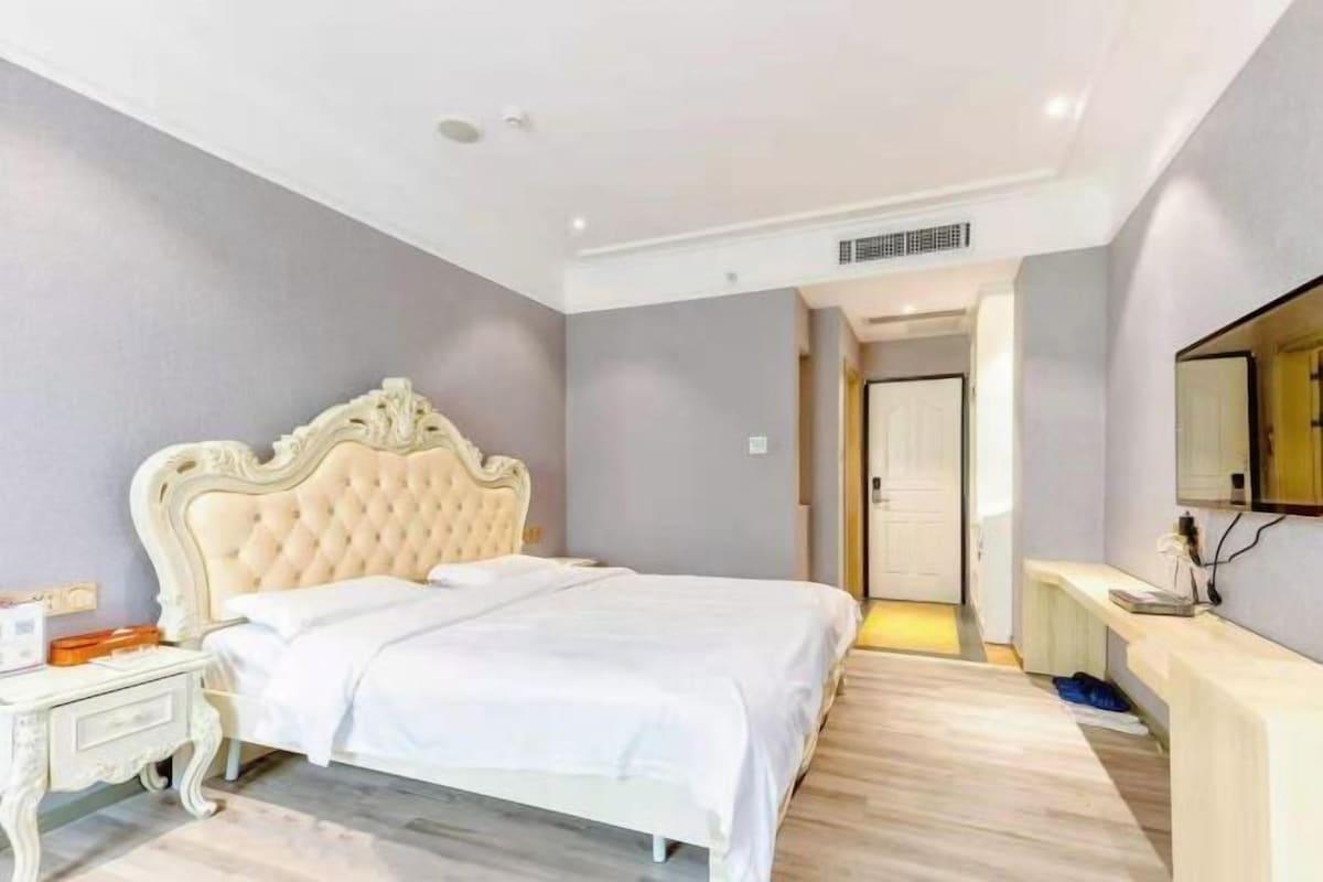 Un dormitorio con un cabecero capitonado, una colcha blanca, una mesita de noche y un espejo en la pared.