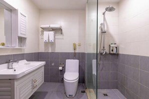 Un baño con lavamanos blanco, inodoro y zona de ducha con mampara de cristal.