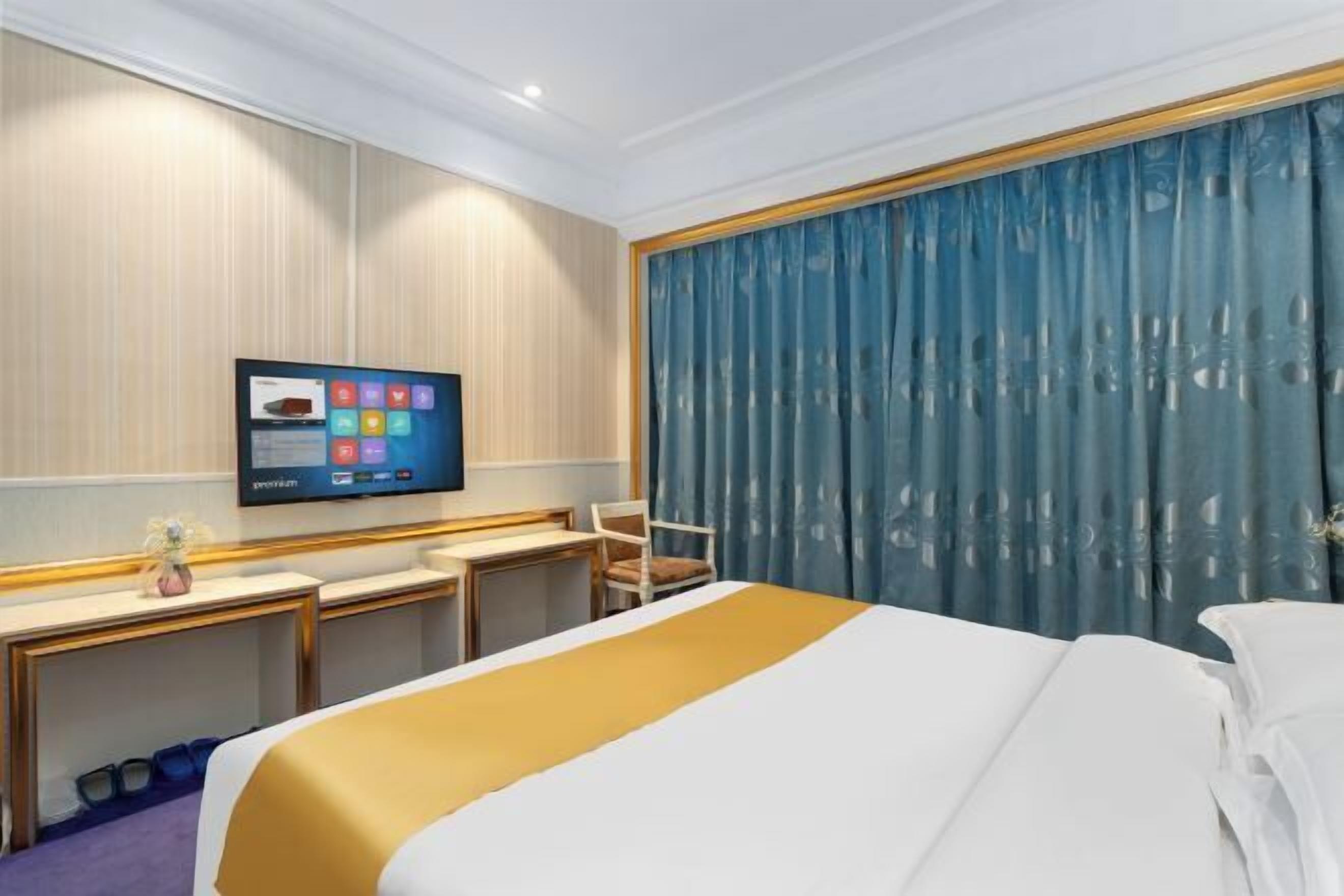 A hotel room with a bed, a desk, a chair, a television, and a large window with curtains.