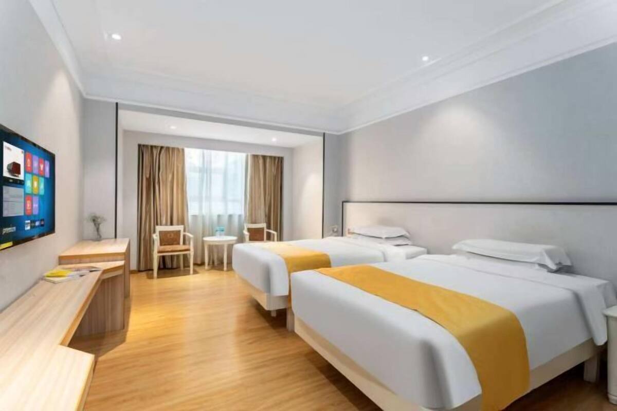 Ein Hotelzimmer mit zwei Betten, einem Schreibtisch, einem Fernseher und einem Fenster mit Vorhängen.