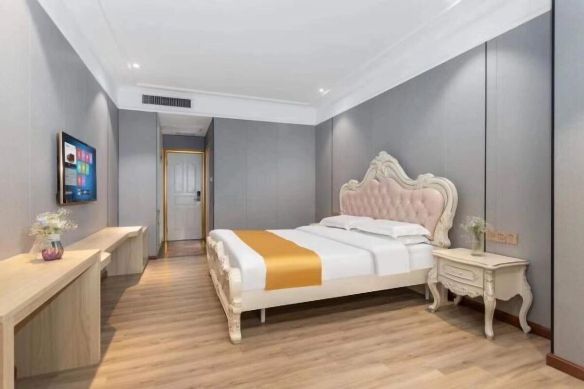 Un dormitorio con cama, mesita de noche y escritorio con un florero.