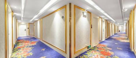 A hotel corridor with a floral carpet, doors on both sides, and overhead lighting.