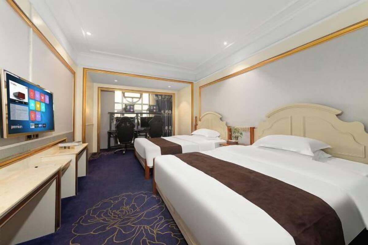 Ein Hotelzimmer mit zwei Betten, einem Schreibtisch, einem Fernseher und Blick auf den Flur.