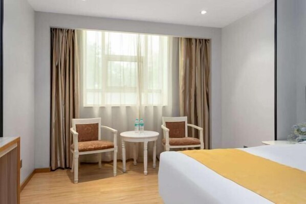 A hotel room with a bed, two chairs, a small table, and a window with curtains.