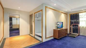 A hotel room with a wooden floor, a blue carpet, a wooden cabinet, a television, and a window with curtains.