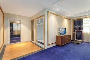 Hotelkamer met houten vloer, blauw tapijt, een houten kast, een televisie en een raam met gordijnen.