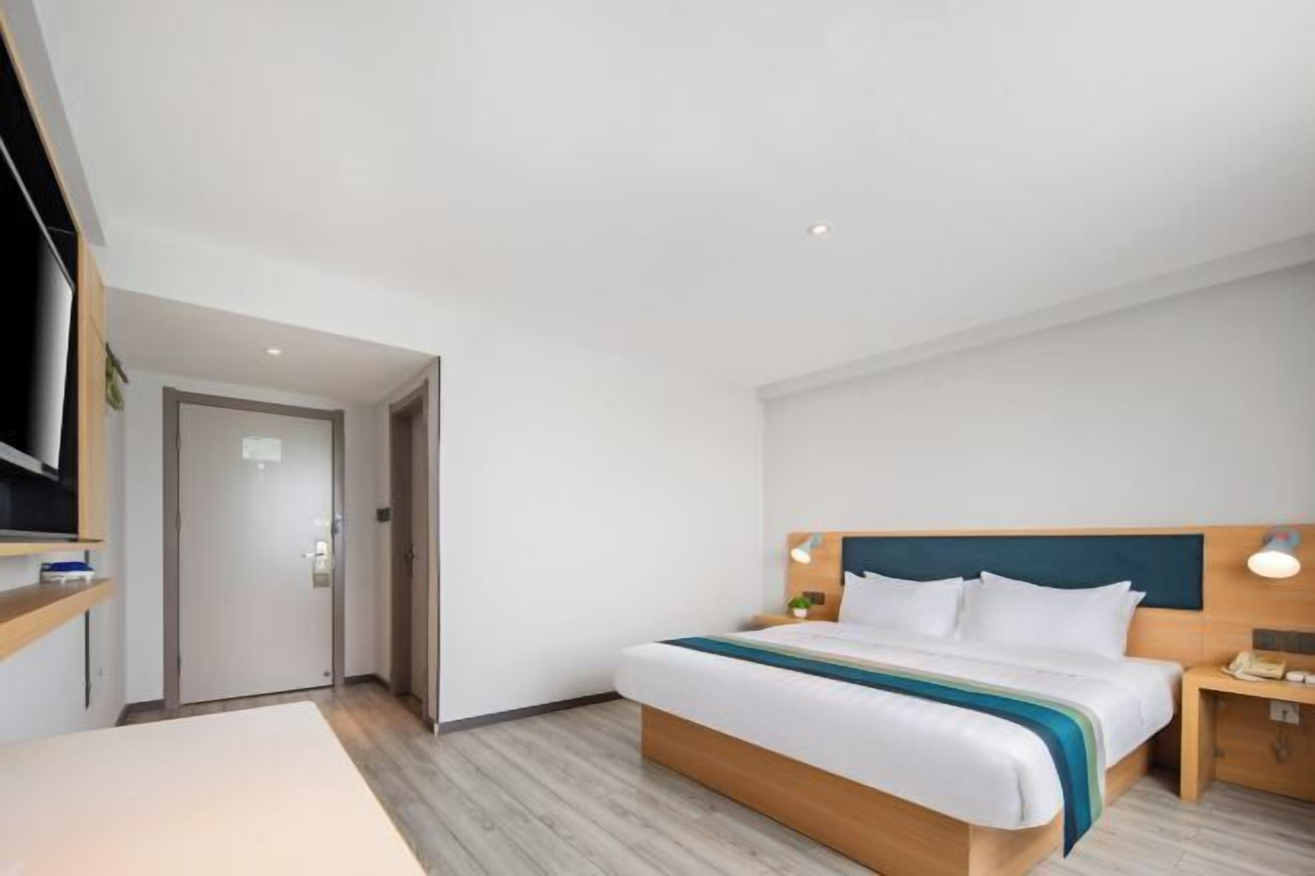 A modern hotel room with a large bed, bedside tables, a TV, and a door leading to another room.