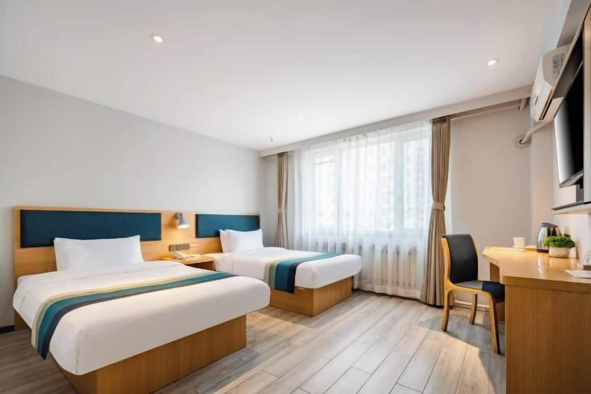 Ein Hotelzimmer mit zwei Betten, einem Schreibtisch, einem Stuhl und einem großen Fenster mit Vorhängen.