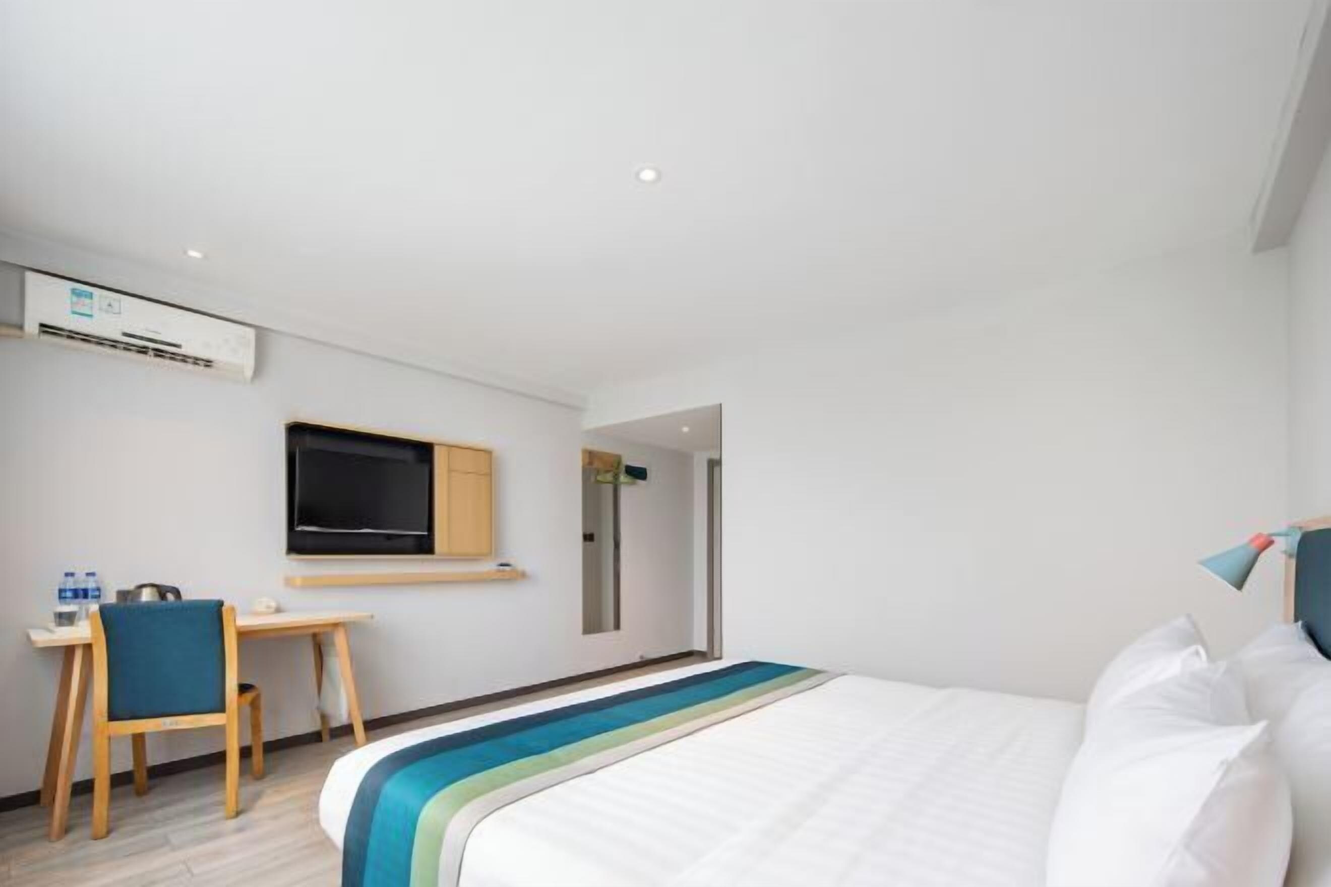 A hotel room with a bed, a desk, a chair, a television, and an air conditioning unit.