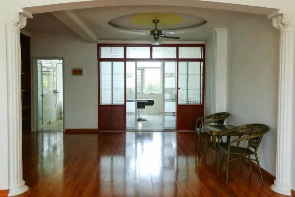 A spacious room with a wooden floor, a ceiling fan, and a large window with a view of the outdoors.