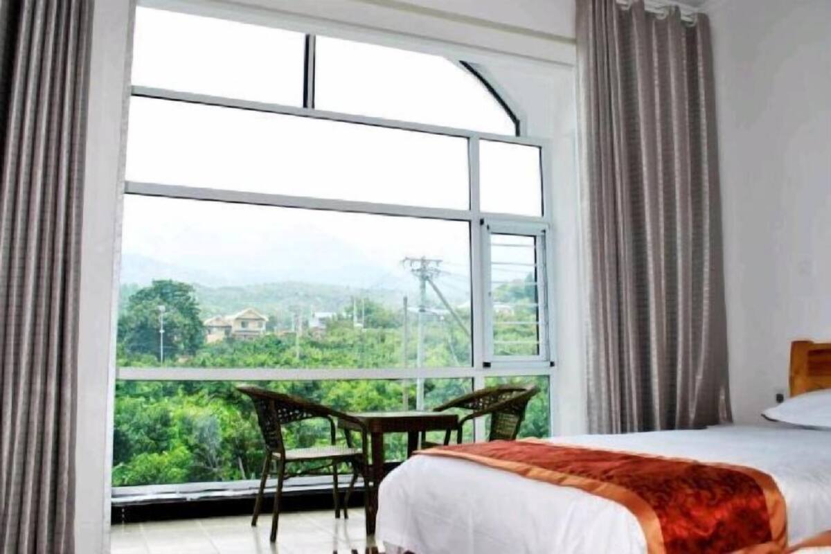 A hotel room with a large window, a bed, and two chairs.