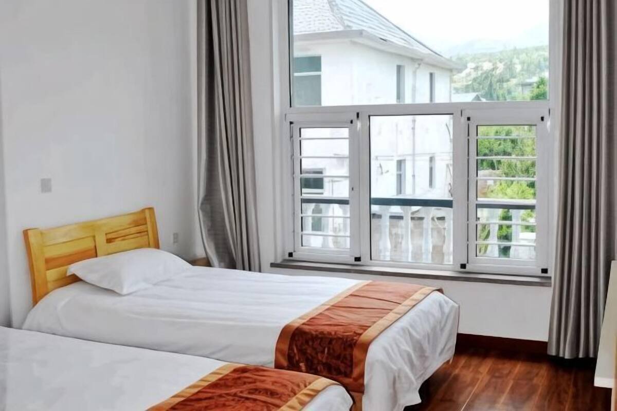 A hotel room with two beds, a large window with curtains, and a view of a balcony.