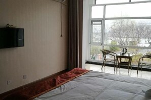 Ein Hotelzimmer mit einem Bett, einem an der Wand befestigten Fernseher, einem Fenster mit Blick nach außen und einem Tisch mit Stühlen.