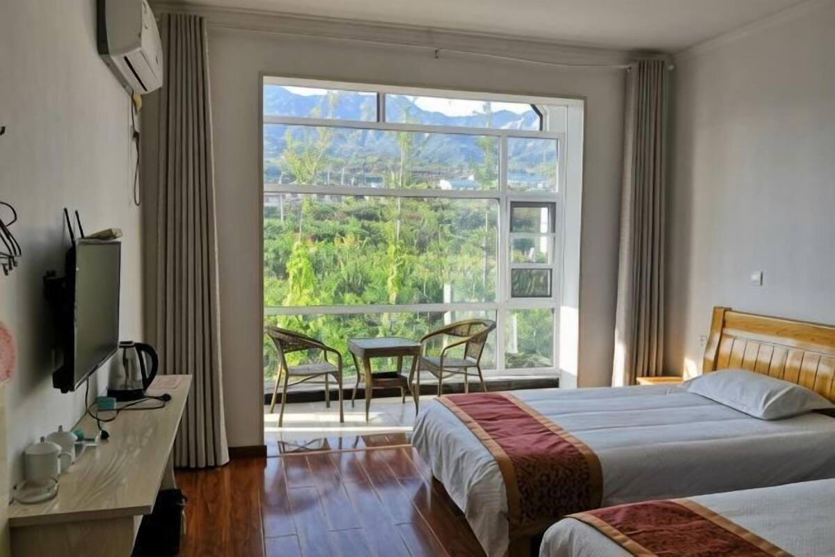 A hotel room with a bed, a desk, a chair, and a view of greenery.