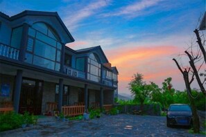 A two-story house with a balcony, a driveway, and a parked car. - Mengyin Yiquan Villa Homestay (Mengyin)