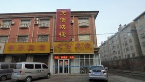 A building with a prominent red sign reading "天浩快捷酒店" and a yellow sign below it. There are two cars parked in front, and the building has multiple windows and balconies. - Gaochun Tianhao Hotel (Gaoyi)