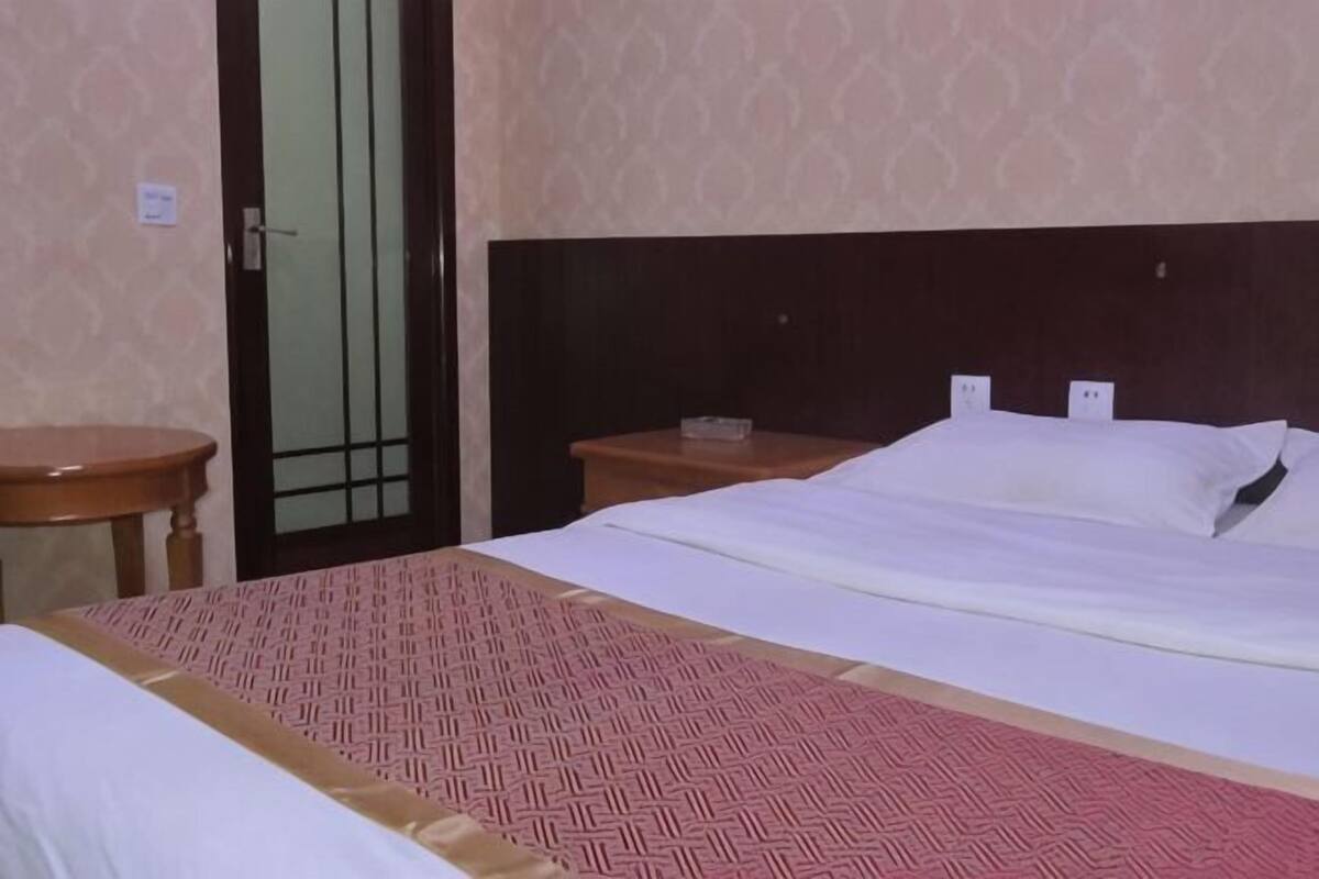 A hotel room with a bed, a bedside table, and a door.