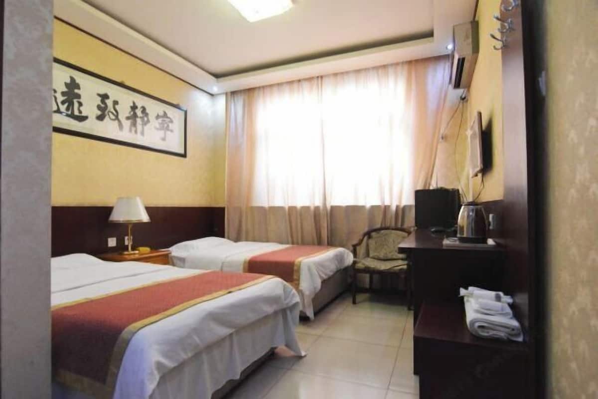 A hotel room with two beds, a desk with a chair, a television, and a window with curtains.