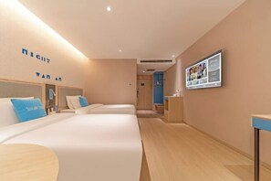 A hotel room with three beds, a wooden floor, a wall-mounted TV, and a reception desk.