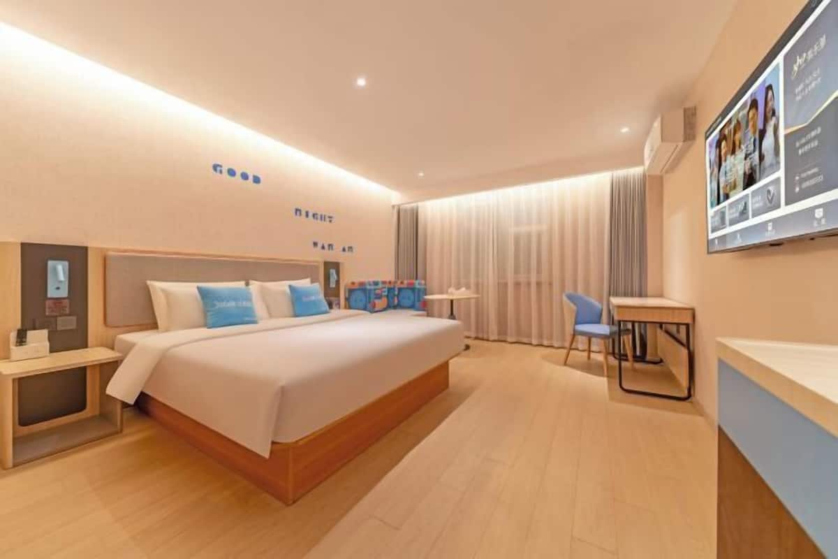 Quarto de hotel moderno com uma cama grande, mesas de cabeceira, escrivaninha e uma cadeira.