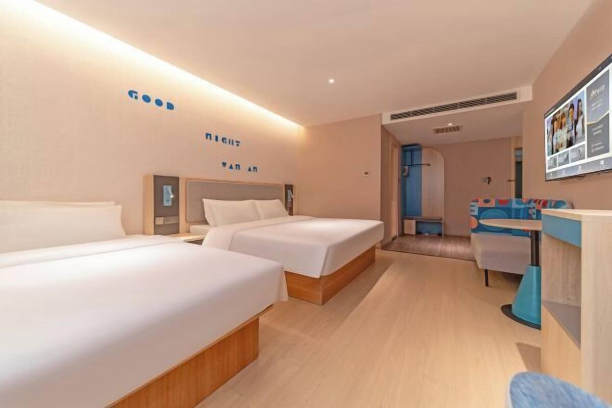 Quarto de hotel com duas camas, uma mesa de trabalho e um pequeno espaço de estar.