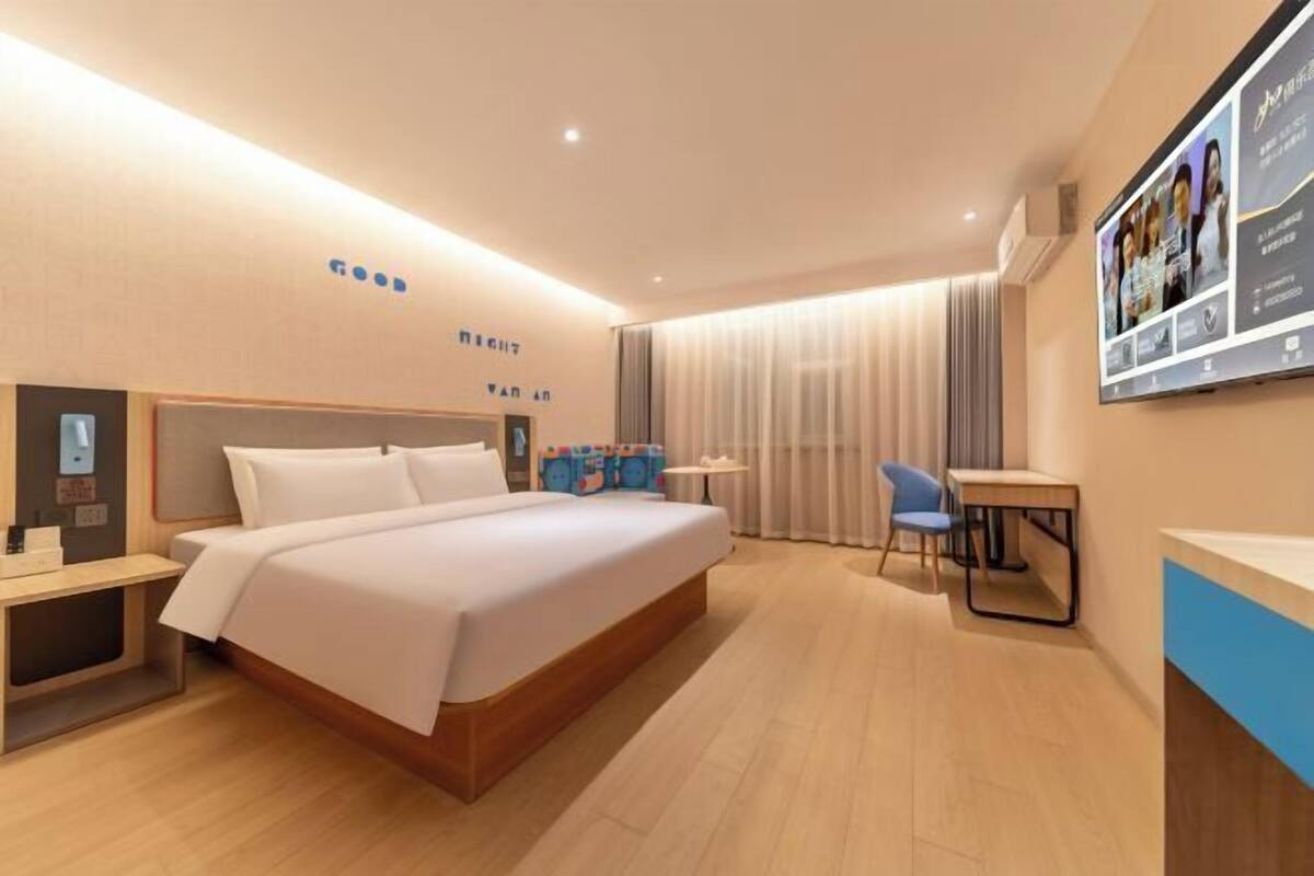 Quarto de hotel moderno com uma cama grande, mesas de cabeceira, escrivaninha e televisão na parede.