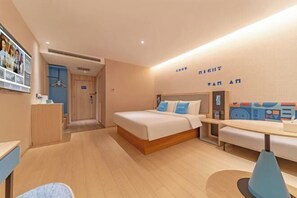 A modern hotel room with a bed, bedside table, and a desk with a chair.