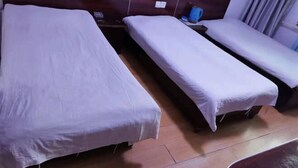 A hotel room with two single beds, a wooden headboard, a small table with a lamp, and a window with curtains.