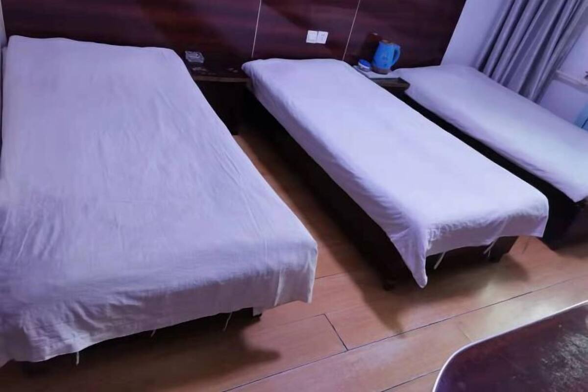 Una habitación de hotel con dos camas individuales, un cabecero de madera, una mesita con una lámpara y una ventana con cortinas.