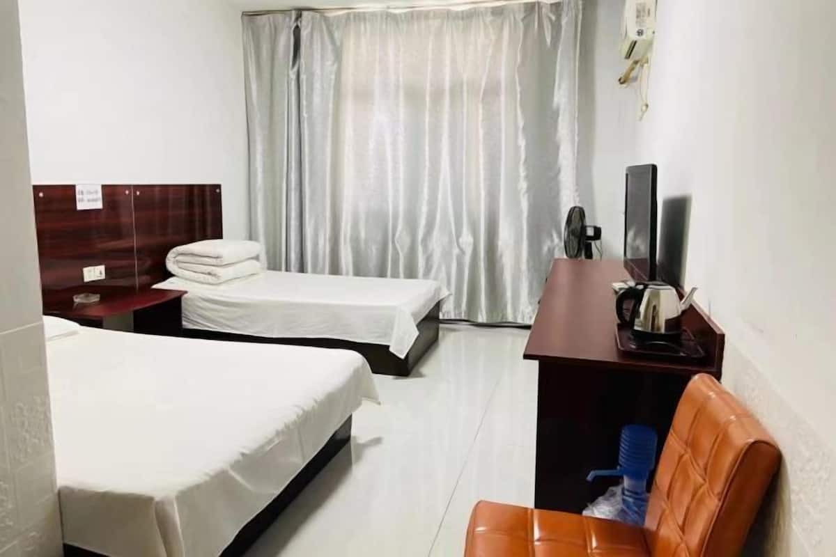 Habitación de hotel con dos camas, un escritorio con hervidor, una silla y una televisión.