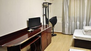 A room with a wooden desk, a television, a standing lamp, a bed, and a window with curtains.
