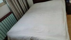 A single bed with a white sheet in a room with a radiator and curtains.