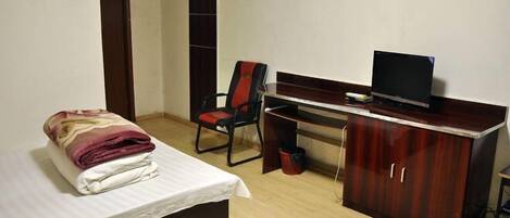 A hotel room with a bed, a desk with a computer, a chair, and a wardrobe.