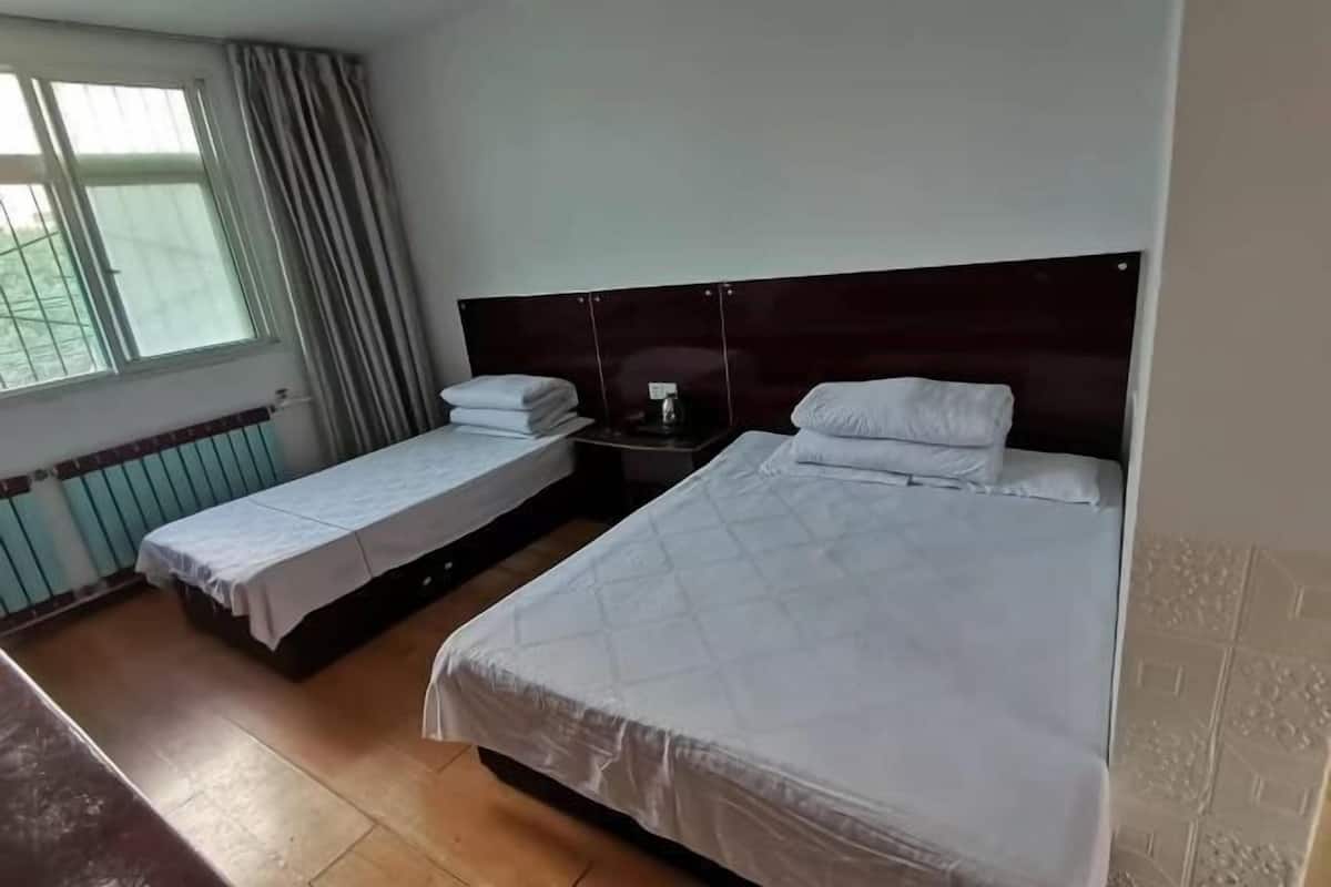 Habitación de hotel con dos camas, una ventana con cortinas, un radiador y una mesita de noche con lámpara.