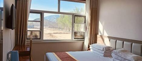 Una habitación de hotel con cama, escritorio, silla, televisor y ventana con vista al exterior.