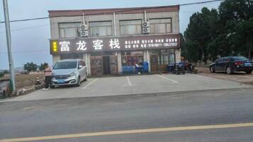A building with a signboard, a parking area, and a few parked vehicles.